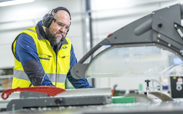 Worker wearing protective gear operating an industrial saw to process plastic material at Etra’s production facility.